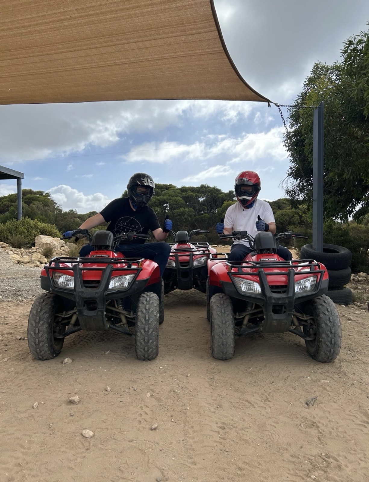 Two riders in helmets and gloves giving a thumbs up from their quad bikes